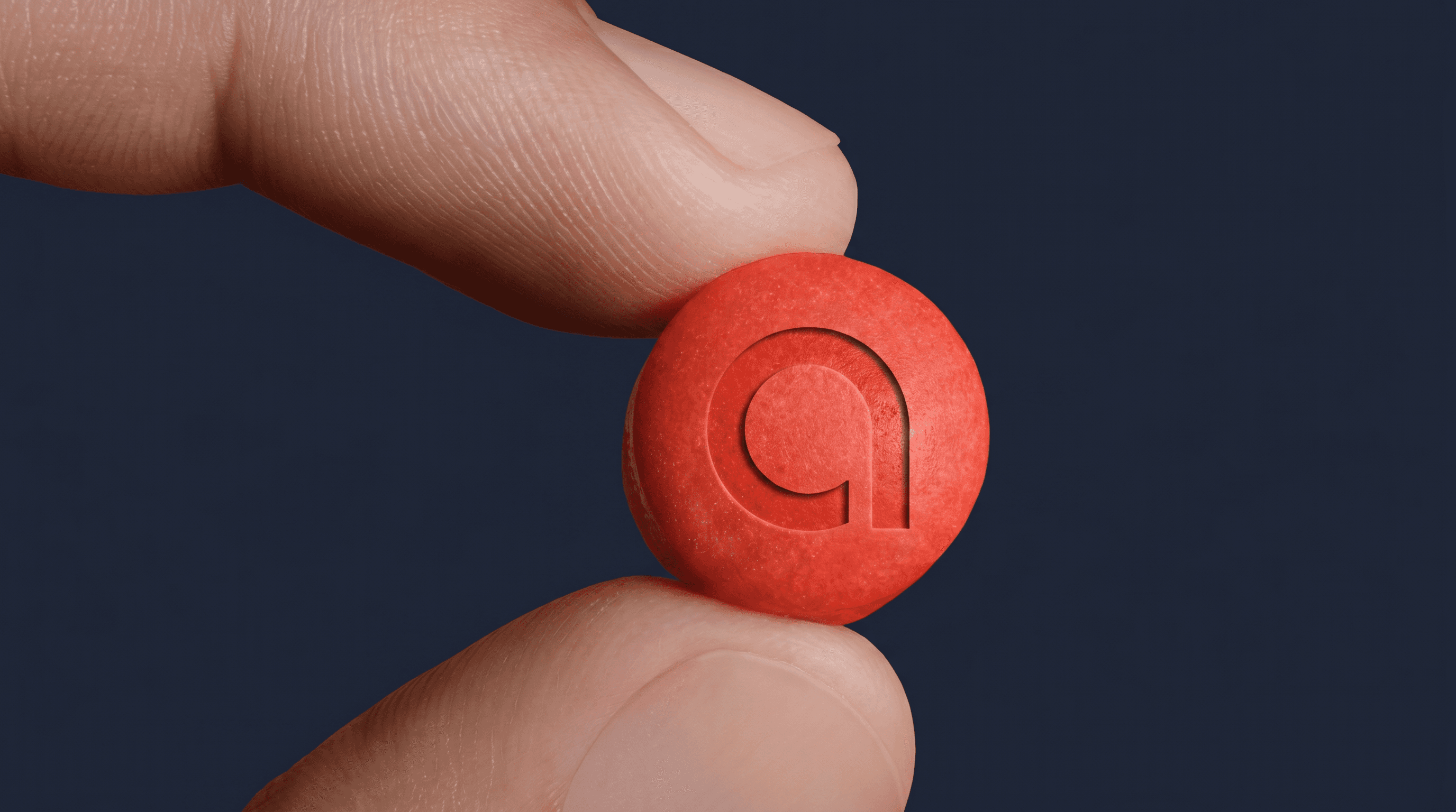 Fingertip holding a red aurameds tablet